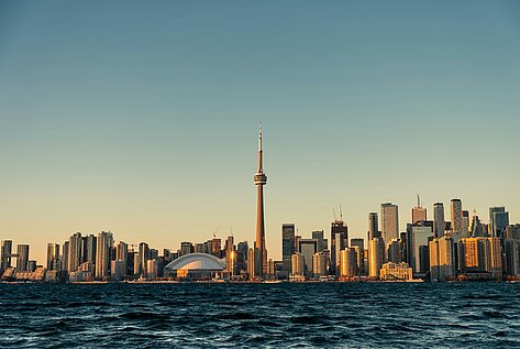 Skyline von Toronto mit CN Tower und Rogers Centre im warmen Abendlicht, aufgenommen vom Wasser aus.