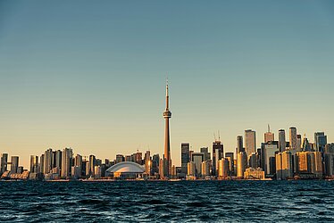 Skyline von Toronto mit CN Tower und Rogers Centre im warmen Abendlicht, aufgenommen vom Wasser aus.