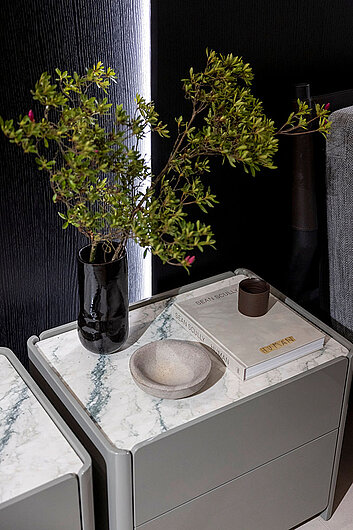 Modernes Möbelmodul mit abgerundeten Kanten und Marmoroptik-Oberfläche, dekoriert mit Vase, Buch und Schale in stilvollem Wohnambiente