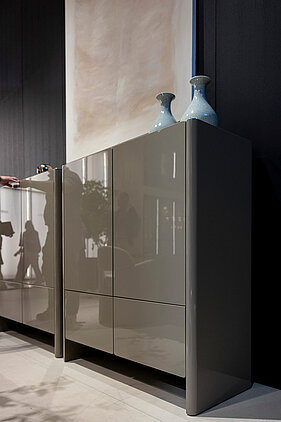 Sideboard mit glänzenden, abgerundeten Fronten in neutralem Farbton, dekoriert mit Vasen im modernen Wohnumfeld