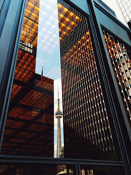 Blick nach oben zwischen Glasfassaden von Hochhäusern in Toronto mit Spiegelungen und sichtbarer CN Tower Spitze.