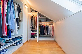 Portrait Begehbarer Kleiderschrank mit schicken MDF-Fronten im geöffneten Zustand mit Blick auf die Kleidung.