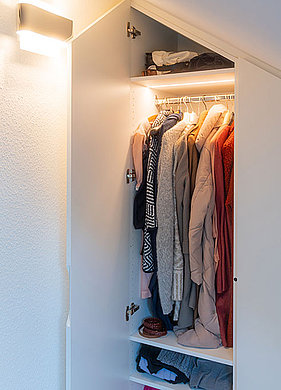 Portrait Begehbarer Kleiderschrank unter der Dachschräge mit geöffneten Türen und Blick auf die Kleidung