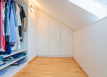 Begehbarer Kleiderschrank mit schicken MDF-Fronten in Weiß und einem Innenleben aus Echtholz unter der Dachschräge.