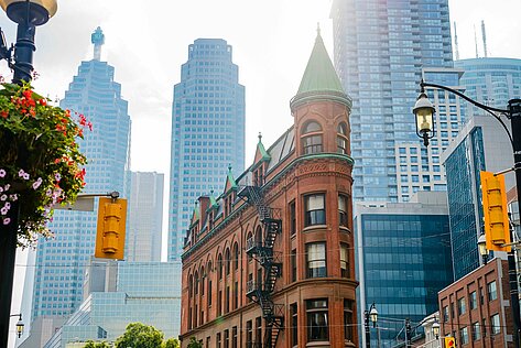 Historisches Backsteingebäude mit Turm in Toronto an einer Kreuzung, umgeben von Glasfassaden und Straßenverkehr im Sommer.